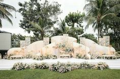 an outdoor wedding setup with white flowers and greenery on the grass, surrounded by palm trees