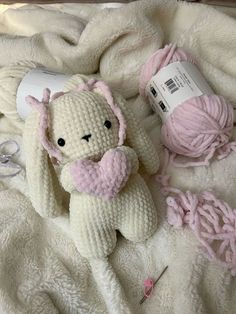 a white stuffed animal sitting on top of a bed next to a ball of yarn