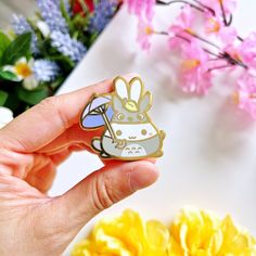 a person holding a small pin with a cartoon animal on it's lap and flowers in the background