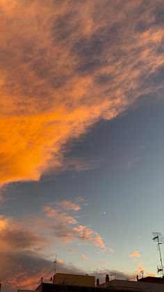 an orange and blue sky at sunset with clouds in the foreground, some buildings to the right