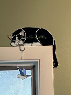 a cat is hanging from the side of a window with a bird decoration on it