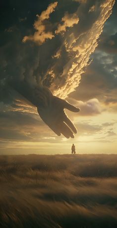 a giant hand reaching into the sky with a person standing in the distance behind it