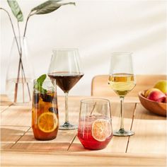 three different types of wine glasses sitting on a wooden table with fruit in the background