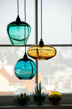 three different colored glass vases hanging from a window sill