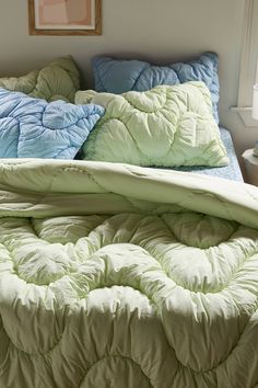 an unmade bed with blue and green comforters in a white room next to a window