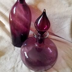 two purple glass vases sitting on top of a white cloth covered tablecloth,