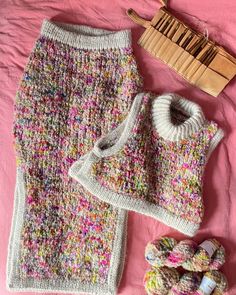 a knitted sweater and skirt are laying on a pink blanket next to some knitting needles