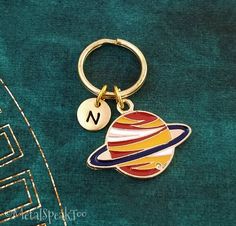 a keychain with the letter n on it and a saturn charm attached to it