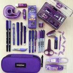 the contents of a purple case are laid out on top of a wooden table, including pens, scissors and other items