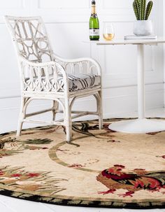 a white chair sitting on top of a rug next to a table with a bottle of wine