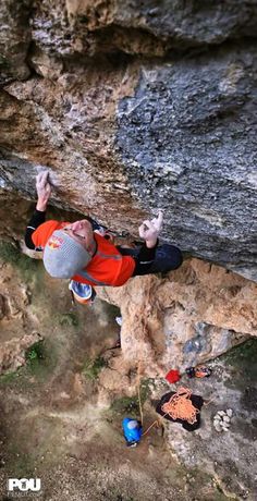 a man climbing up the side of a cliff with his hands in the air while wearing an orange and black jacket