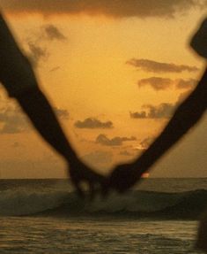 two people holding hands while standing in front of the ocean at sunset with waves behind them