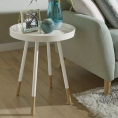 a small white table with two vases on it and a couch in the background