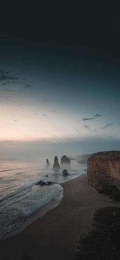 the beach is next to some rocks and water at dusk with clouds in the sky