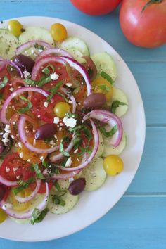 a white plate topped with cucumbers, tomatoes and onions