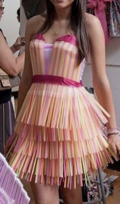 a woman standing in front of a mirror wearing a dress made out of paper strips