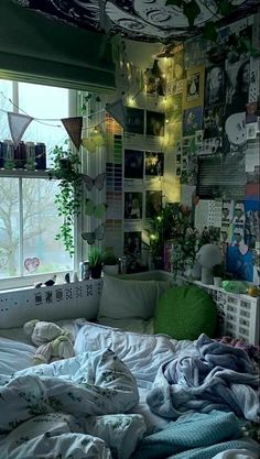 an unmade bed sitting in front of a window with lots of pictures on the wall