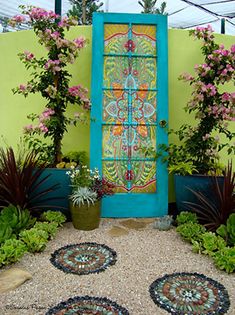 an outdoor area with potted plants, flowers and a blue door in the middle