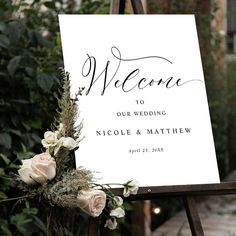 a welcome sign sitting on top of a wooden easel next to flowers and greenery