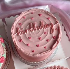 a pink birthday cake with hearts and the words happy birthday on it next to two other cakes