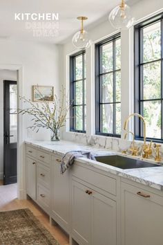 a kitchen with white cabinets and marble counter tops, gold faucets, and black framed windows