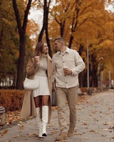 a man and woman walking down a sidewalk in the fall with leaves on the ground