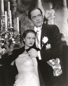 an old black and white photo of a man in a tuxedo standing next to a woman