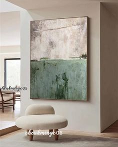 an abstract painting hangs on the wall above a white chair and ottoman in a living room