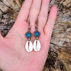 two white and blue shell earrings on a person's hand