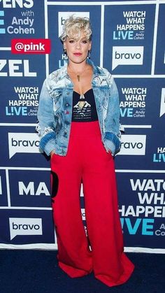 a woman in red pants and denim jacket standing on a blue carpet with her hands in her pockets