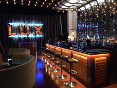 a dimly lit bar with stools and lights on the wall in front of it