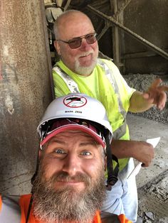 two men in safety vests and hard hats posing for a photo with each other