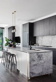 a kitchen with marble counter tops and stools in front of an open floor plan