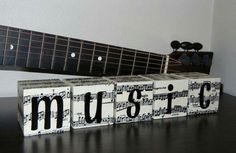 the word music spelled out with blocks in front of an acoustic guitar and wall hanging