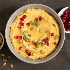 a bowl filled with hummus, pumpkin seeds and cranberries