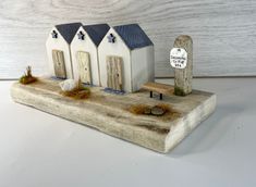 a small white house sitting on top of a piece of wood next to a sign