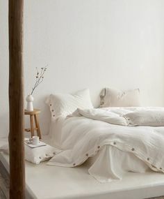 a bed with white linens and pillows in a room that has wood flooring