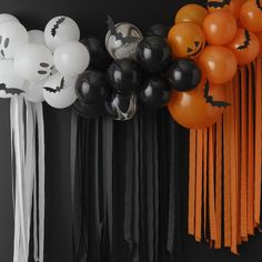 halloween decorations and balloons are hanging on the wall in front of a black backdrop with white, orange and black balloons