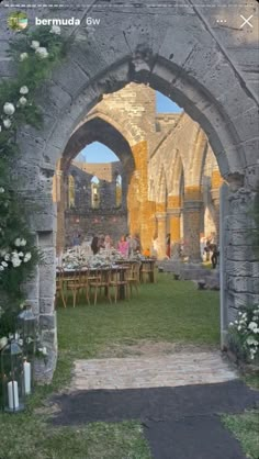 an archway with flowers growing on it and people sitting at tables in the background outside