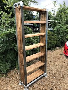 a wooden book shelf sitting in the middle of a garden next to a red car