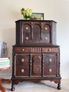 an old wooden cabinet sitting next to a table with flowers on top and books stacked on it