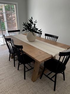 a wooden table with black chairs and a white vase