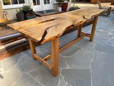 a wooden table sitting on top of a stone floor next to a bench and potted plant