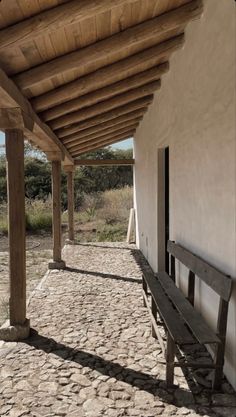 a wooden bench sitting on the side of a white building next to a stone walkway