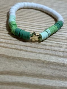 a green and white beaded bracelet with gold clasp on a wooden surface, close up