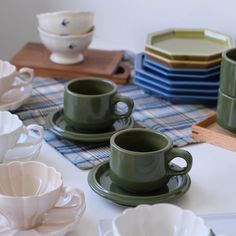 green cups and saucers sitting on top of a table next to other plates, bowls and napkins