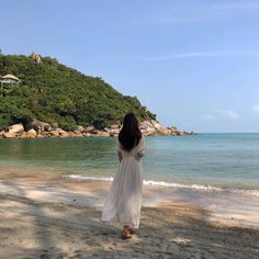 a woman standing on top of a sandy beach next to the ocean with a hill in the background