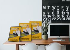 a desk with a computer and calendars on it, along with two white chairs