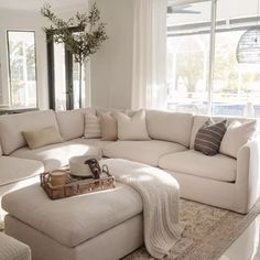 a living room with a large white sectional couch and coffee table in front of two windows