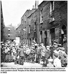 an old black and white photo of people standing in front of brick buildings with children on the sidewalk